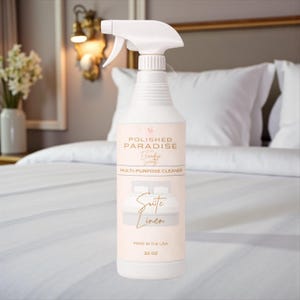 May include: A white spray bottle of "Suite Linen" multi-purpose cleaner from Polished Paradise Co. The bottle has a white spray nozzle and a label with text and a bed illustration. The bottle contains 32 oz of cleaner.
