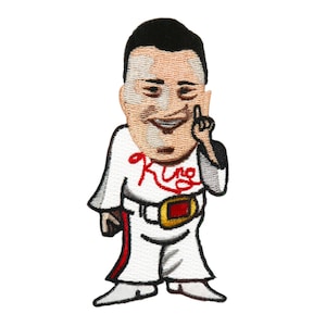May include: Embroidered iron-on patch featuring a cartoon man with a white suit, red belt, and the word "King" in red lettering on his chest. He is smiling and pointing with his right index finger.