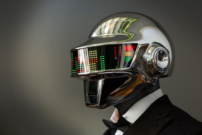 May include: A chrome-finished helmet with a visor displaying a colorful graphic equalizer. The helmet is part of a costume, worn with a black tuxedo and bow tie. The design is futuristic and reminiscent of electronic music artists.