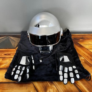 May include: A silver chrome helmet with a black visor, accompanied by a pair of black gloves with reflective silver accents. The items are displayed on a black velvet bag, suggesting a costume or performance theme.