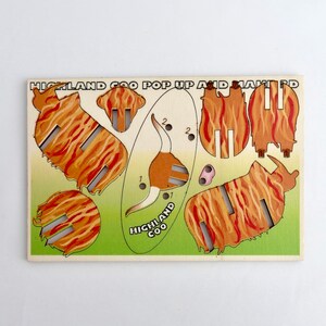K&ouml;nnte beinhalten: Ein Vintage-Papierbastelset mit einer Highland-Coo, einer schottischen Rinderrasse. Das Set enth&auml;lt verschiedene Teile, um ein 3D-Modell des Tieres zusammenzubauen. Die Teile sind nummeriert und mit Anweisungen zum Zusammenbau beschriftet. Das Set tr&auml;gt den Titel "Highland Coo Pop Up and Make It".