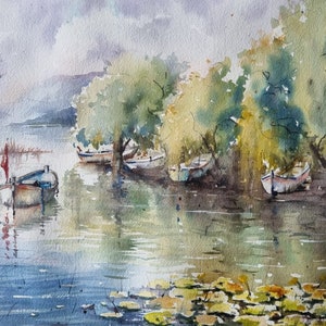 May include: Watercolour painting of a lake scene with several small boats moored under a canopy of trees. The water is calm and reflects the sky and trees. There are lily pads in the foreground.