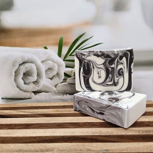 May include: Two bars of handmade soap with a black and white marbled design. The soap is sitting on a wooden surface.