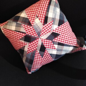 May include: A red, white, and blue plaid pillow with a starburst design. The pillow is made from fabric scraps and has a rustic, handmade look.