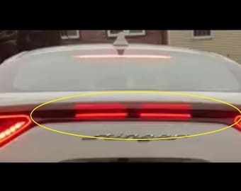 May include: A white car with a black rear spoiler and red taillights. The car has a black rear bumper and a black license plate.