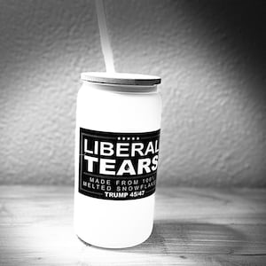 May include: White tumbler with a lid and straw. The tumbler has a black label with the words "LIBERAL TEARS" and the text "MADE FROM 100% MELTED SNOWFLAKE TRUMP 45/47".