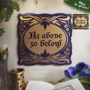 Könnte beinhalten: Ein Holzschild mit einem violetten und goldenen Rahmen und einer ovalen goldenen Mitte mit dem Text "As above so below" in schwarzen Buchstaben.