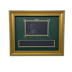 May include: A rectangular picture frame with a gold-colored, ornate border. The frame has a green interior with two rectangular openings and a gold-colored inner border. The frame is designed to hold photographs or artwork.