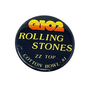 May include: A black button with a yellow and orange logo that says "8102" and "ROLLING STONES" in white text. The button also says "ZZ TOP, COTTON BOWL - 81" in white text.