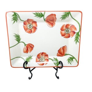 Peut inclure: Plat à servir rectangulaire en céramique avec un fond blanc, orné de fleurs de coquelicots orange et de feuilles vertes. Le plat a une bordure orange et est présenté sur un support en métal noir. Une pièce décorative pour servir des aliments.