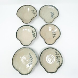 May include: Set of six white ceramic dipping bowls with a blue rim and a blue leaf design. The bowls have a slight curve and a small indentation on one side.