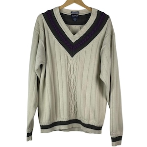 Pode incluir: Um suéter bege com decote em V com um design de malha de cabo no centro e detalhes listrados. O suéter tem listras verdes escuras e roxas ao redor da gola e da bainha. A marca "GANT" é visível.