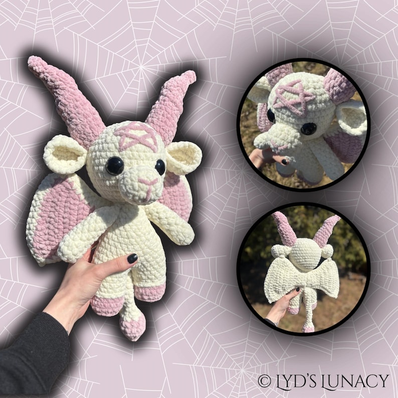May include: A white crocheted goat with pink wings and horns. The goat has a pentagram on its forehead and large black eyes. The goat is being held by a hand.