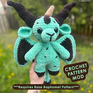 Puede incluir: Un peluche de ganchillo con forma de criatura mítica, con cuerpo turquesa y detalles negros en alas, cuernos y pezuñas. Tiene grandes ojos negros y un cuerno marrón. El texto "CROCHET PATTERN MOD" y "Requires Base Baphomet Pattern" son visibles.