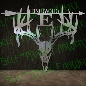 May include: A metal wall art piece featuring a deer skull with antlers, an arrow, and the name "EINERWOLD" above the letter "E". The artwork is in a silver color and is designed for wall decor.