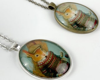 May include: Two oval-shaped necklaces with a squirrel wearing a hat and sweater on each pendant. The pendant on the left has a silver chain and the pendant on the right has a bronze chain.