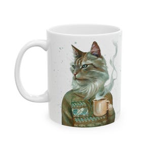 May include: A white ceramic mug featuring a detailed illustration of a long-haired ginger cat wearing a brown patterned sweater. The cat is holding a small beige mug with a wisp of steam rising from it, set against a white background with speckles.