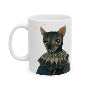 May include: A white ceramic mug featuring a detailed illustration of a dark-furred bat with large, reflective brown eyes. The bat is wearing a dark, patterned collar with small buttons. The background of the illustration has subtle speckles.