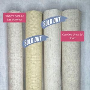 May include: Four vertical rolls of fabric for needlework. The first roll is labelled Fiddler's Aida 14 Lite Oatmeal. The second and third rolls have blue text overlays reading SOLD OUT. The fourth roll is labelled Carolina Linen 28 Sand.