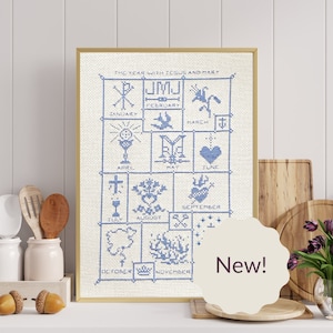 May include: A framed cross-stitch design with blue embroidery on a white background. The design features a calendar with each month represented by a different religious symbol. The text "The Year with Jesus and Mary" is at the top of the design. The word "New!" is written in a white circle on a beige background.