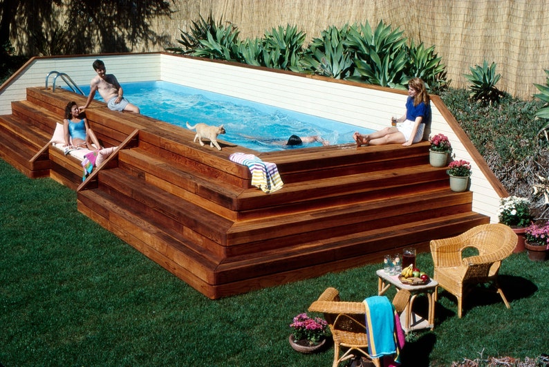 May include: A wooden deck with a swimming pool and steps leading down to the water. There are people relaxing on the deck and in the pool.