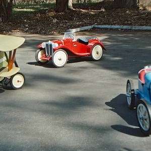 Puede incluir: Tres veh&iacute;culos de juguete, un roadster rojo, un coche de carreras azul y un biplano verde y blanco, est&aacute;n alineados en una superficie de asfalto gris.