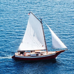 May include: A white sailboat with a red hull and a white sail. The boat is sailing on a blue body of water.
