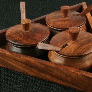 May include: A triangular wooden tray with three small wooden bowls with lids and spoons. The bowls are made of dark wood and have a natural finish. The tray is perfect for serving spices or condiments.
