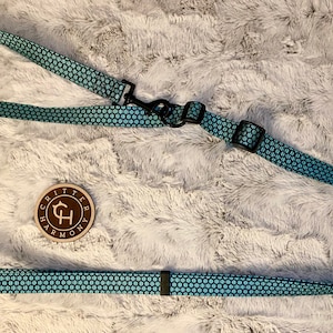 May include: A blue and black dog leash with a honeycomb pattern. The leash has two clips and a brown leather tag with the text "Critter Harmony" and a stylized "CH" logo.