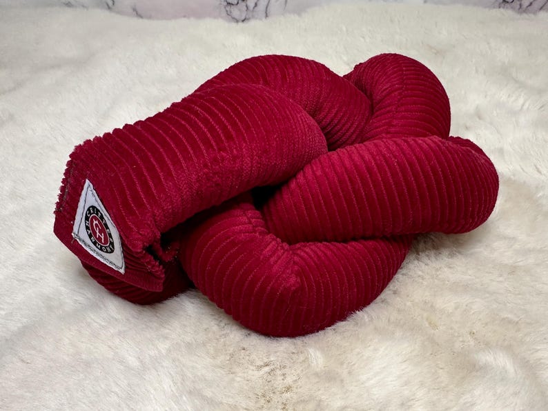 May include: A red corduroy knot pillow with a white label that says "Cozy Knots".