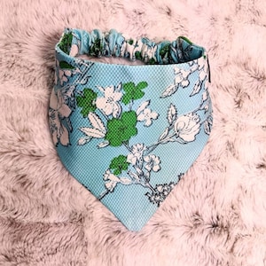 May include: A light blue bandana with a white and green floral pattern. The bandana has an elastic band around the top.