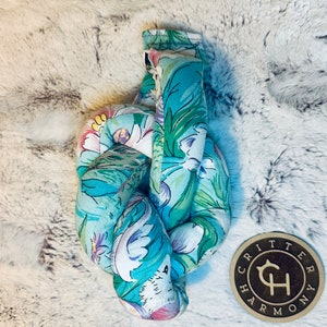 May include: A knotted, teal blue and white floral fabric dog toy with a brown wooden tag that says "Critter Harmony" in a stylized font.