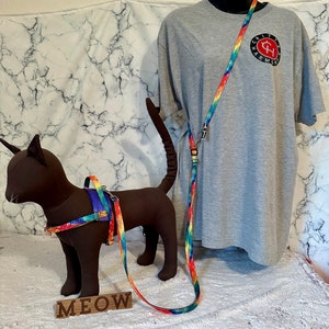 Puede incluir: Un conjunto de arnés y correa para gato con estampado tie-dye arcoíris y una camiseta tie-dye a juego. El arnés y la correa están hechos de cinta de nylon resistente y cuentan con un clip de metal. La camiseta está hecha de algodón suave y presenta un logotipo en la parte delantera. El conjunto es perfecto para llevar a tu gato a pasear o de aventuras.