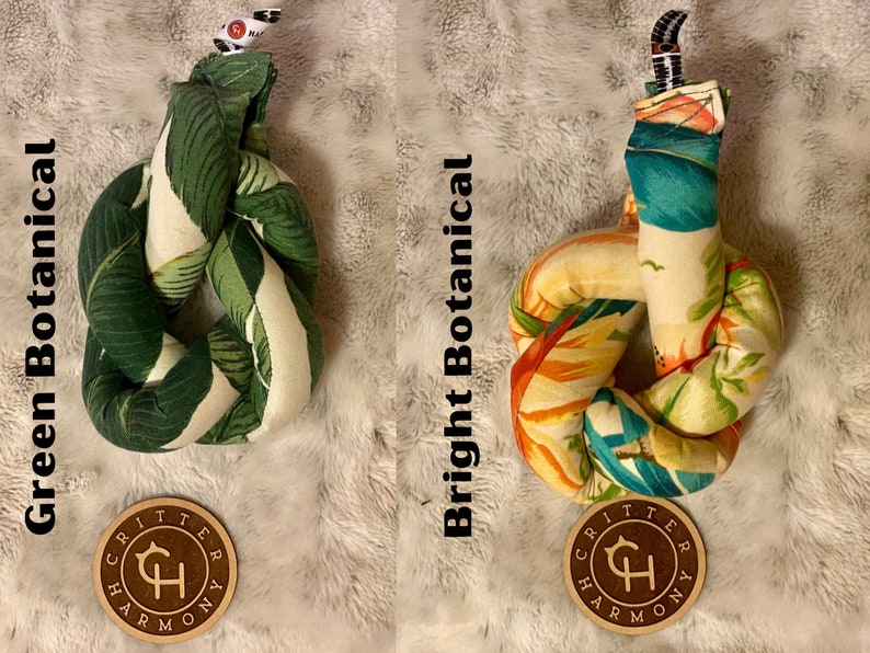 May include: Two knotted dog toys with a tropical leaf print. The toy on the left has a green and white leaf print and is labeled "Green Botanical". The toy on the right has a bright orange, yellow, and blue leaf print and is labeled "Bright Botanical". Both toys have a brown circular tag with the text "Critter Harmony" and a stylized "CH" logo.