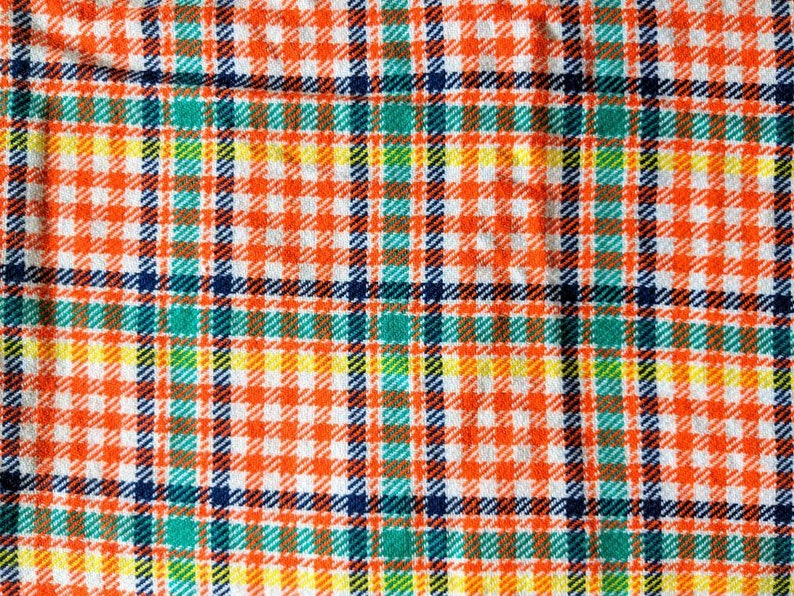 May include: A close-up of a fabric with a plaid pattern in orange, white, blue, green, and yellow.