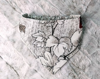 May include: A white and gray bandana with a floral pattern featuring white leaves on a gray background. The bandana has a ruffled edge.