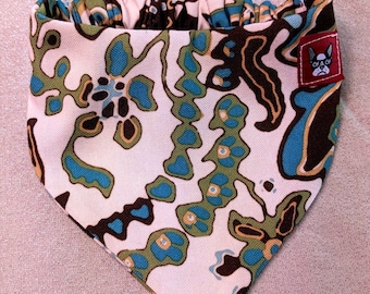 May include: A white bandana with a brown, blue, and green abstract pattern. The bandana has a gathered elastic band at the top and a small red patch with the text "CHA CHA" and a cartoon dog wearing sunglasses.