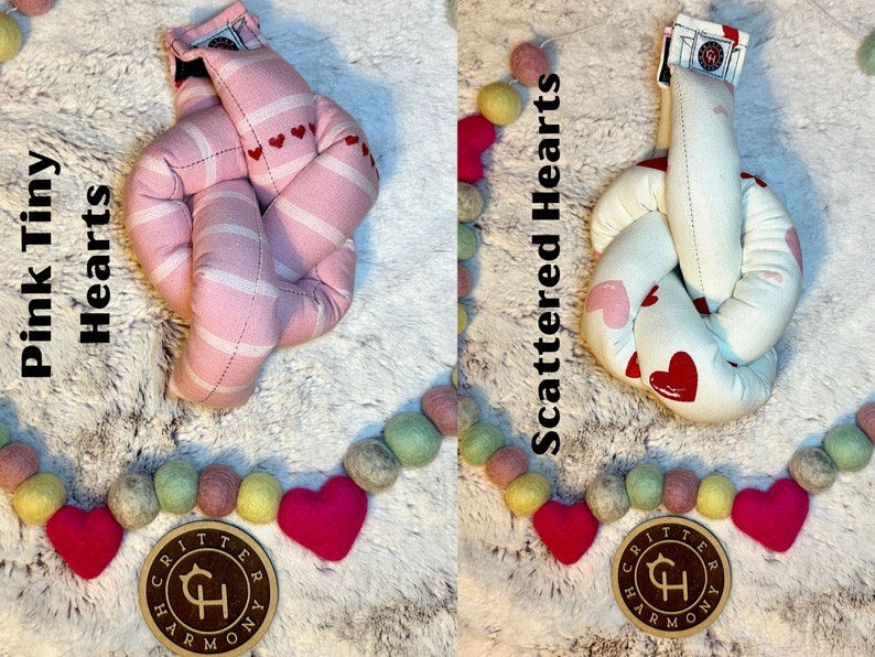 May include: Two knotted fabric heart-shaped toys. The toy on the left is pink with white stripes and small red hearts. The toy on the right is white with scattered pink and red hearts. Both toys have a brown tag with the text "Critter Harmony" and a stylized "CH" logo.