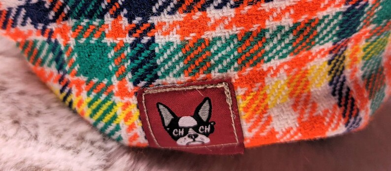 May include: A red, white, and blue plaid fabric with a small patch featuring a black and white bulldog with the text "CH CH" on its collar.