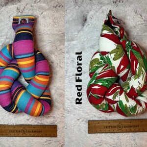 May include: Two knotted dog toys, one with a multi-colored striped pattern and the text "Fiesta" and the other with a red floral pattern and the text "Red Floral".