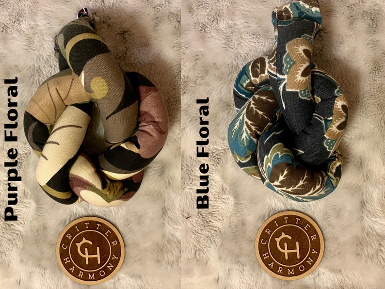 May include: Two knotted dog toys with floral patterns. The toy on the left has a purple floral pattern and the toy on the right has a blue floral pattern. Both toys have a brown leather tag with the text "Critter Harmony" and a stylized "CH" logo.