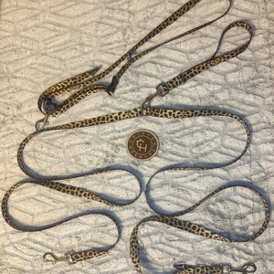 May include: Three leopard print dog leashes with silver clips and a brown leather tag with the text "Critter Harmony" and a stylized letter "H".