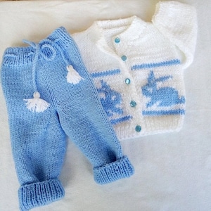 Può includere: Un set di abbigliamento in maglia per neonati in blu e bianco. Il set comprende un cardigan con un motivo a coniglio e bordatura blu, e pantaloni abbinati con frange bianche.
