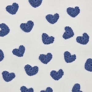 May include: A collection of small, blue, crocheted heart-shaped appliques scattered across the frame. Each individual heart is crafted from yarn with a visible, textured stitch pattern, creating a uniform appearance across all pieces.