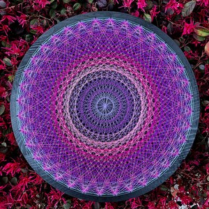 Puede incluir: Una pieza circular de arte de cuerda con un diseño de mandala en tonos de rosa, morado y blanco. El arte se crea con cuerda envuelta alrededor de clavos martillados en una tabla de madera.