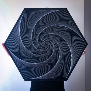 May include: A black hexagonal wall art piece with a white string art design of a spiral. The spiral is made of many thin lines that create a hypnotic effect.