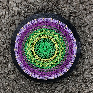 May include: A circular string art piece with a black wooden frame. The string art features a multi-coloured design with concentric circles of purple, green, and yellow thread.