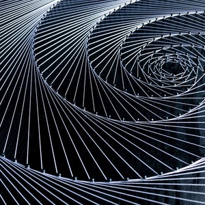 May include: A close-up of a string art piece with a spiral design. The string is white and the background is black. The string is wrapped around nails that are hammered into the black surface.