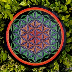 May include: A circular wall hanging featuring a geometric pattern in shades of green, orange, and purple. The pattern is a flower of life design, a sacred geometry symbol.