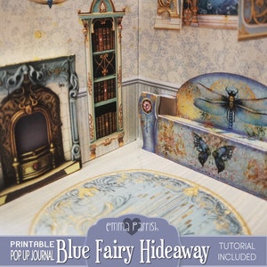 Puede incluir: Un diario desplegable imprimible titulado "Blue Fairy Hideaway" con un tutorial incluido. El diario presenta un dise&ntilde;o de tem&aacute;tica de hadas caprichoso con una combinaci&oacute;n de colores azul y dorado. La imagen muestra una escena desplegable en 3D de una habitaci&oacute;n con una chimenea, una estanter&iacute;a y un banco.